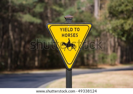Yellow horse crossing yield sign next to road