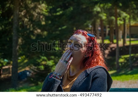 Young pretty and cute redhead girl with Rastafarian theme yawning in the nature 
