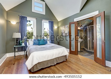 High vaulted ceiling bedroom interior design. There is large bed , opened doors to bathroom, gray walls and hardwood floor in the room. Northwest, USA