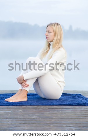 Young woman relaxing after gymnastics in the mist on the lake footbridge early morning. Peaceful atmosphere. Foggy air.