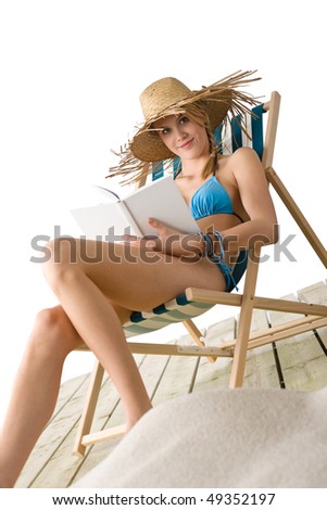 Beach - Happy young woman relax with book sitting on deck chair in bikini with straw hat
