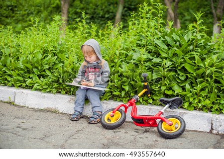 Little boy reading a book under big linden tree, homeschooling concept