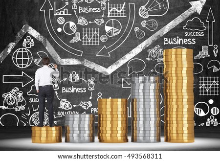 Rear view of man standing on stack of coins against blackboard with white graph and business icons. Concept of becoming wealthy