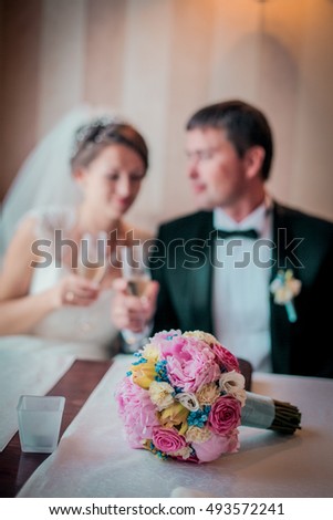  Groom and bride drink champagne in vintage cafe. Man in bowtie and suit. Woman in white wedding dress with veil.