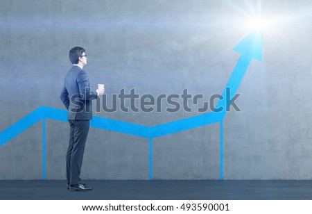 Side view of businessman with paper cup of coffee examining blue graph on gray wall. Concept of statistics and data presentation. Mock up. Toned image