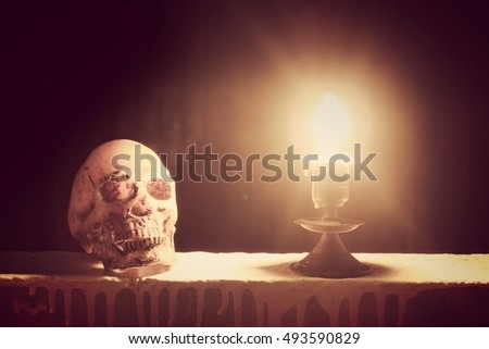 Candle and candle light with skull in dim light in night time with black background.