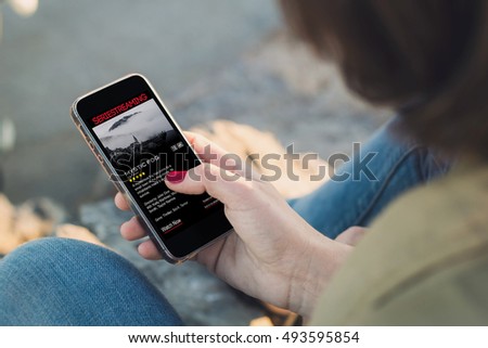 woman holding a smartphone and touching the screen showing series streaming website. All screen graphics are made up.