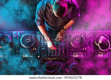 Charismatic disc jockey at the turntable. DJ plays on the best, famous CD players at nightclub during party. EDM, party concept. Royalty-Free Stock Photo #493623178