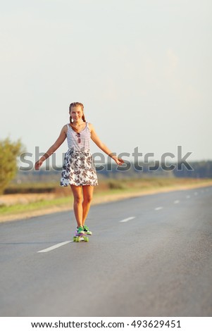 Young happy cute girl rides skateboard on road, outdoor