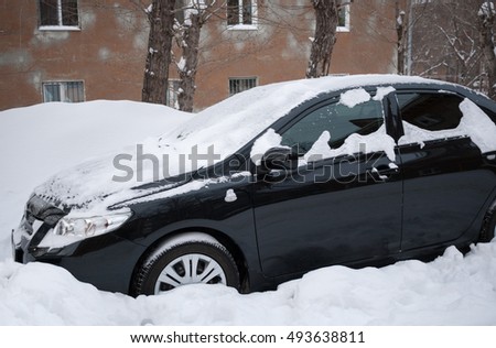 Black car covered with snow standing in snow near the house. Winter picture.