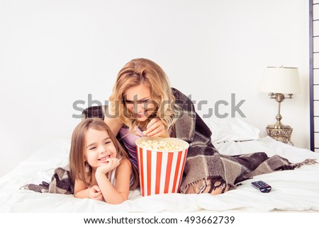 Portrait of happy mother and her daughter watching cartoons with popcorn in bed