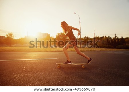 Beautiful young girl with tattoos riding longboard in sunny weather
