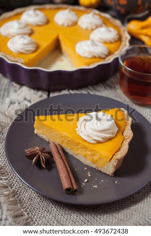 Festive Thanksgiving Homemade Pumpkin Pie with Whipped Cream on wooden rustic background with spices and tea