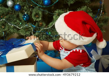 Cute little boy in santa hat holding a gift near Christmas tree. child with present. xmas kid