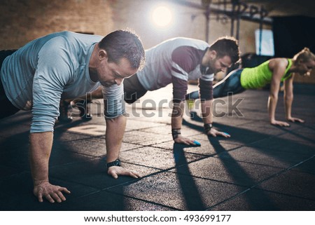 Group of adults performing push up exercise drills at indoor physical fitness cross-training exercise facility with bright light flare over them Royalty-Free Stock Photo #493699177