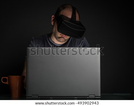 Technology addicted man at home at night on gray background. Virtual reality addiction concept.