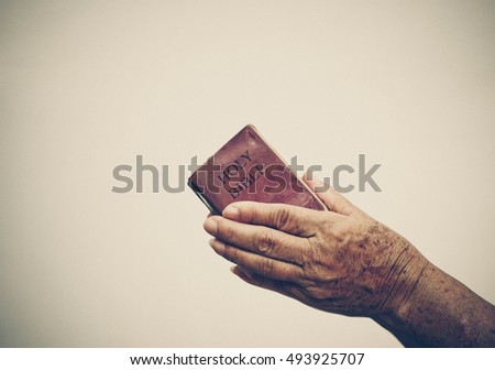 Old female hand holding an old small book of bible