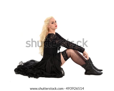 beautiful blonde woman wearing a long black gothic gown, sitting on the ground.  isolated on white background.