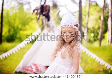 Girl in indian costume with white feather band wearing on her head, wigwam tent at background
