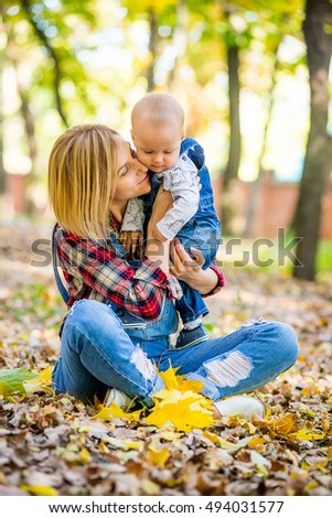 Happy young mother playing with baby in autumn park with yellow maple leaves. Family walking outdoors in autumn. Little boy with her mother playing in the park in autumn.