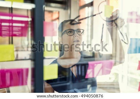View through a glass wall. Creative woman use post it notes to share idea. Modern business office Royalty-Free Stock Photo #494050876