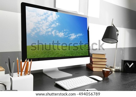 Comfortable workplace with modern computer and green spring field on screen