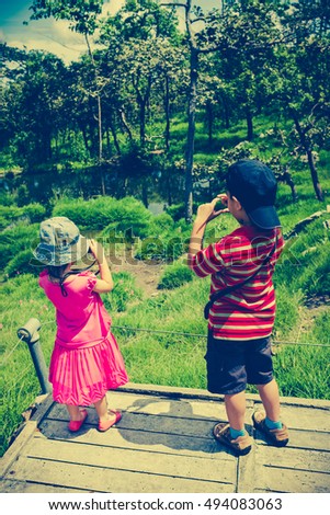 Back view of asian children taking photos by camera at national park . Family relaxing outdoors at the daytime, travel on vacation. child in nature. Cross process and vintage tone effect.