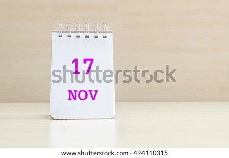 Closeup surface note book with purple 17 nov word in page on blurred brown wood desk and wood wall textured background with copy space under window light