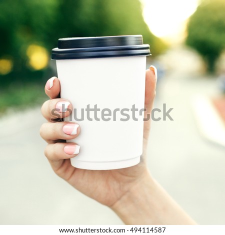 hand holding paper cup of coffee on natural morning background