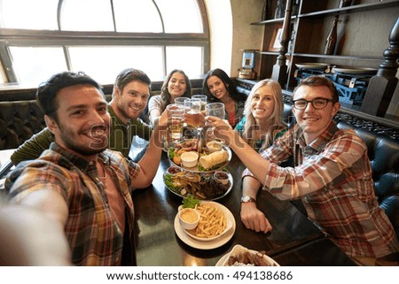 people, leisure, friendship and technology concept - happy friends taking selfie, drinking beer and eating snacks at bar or pub