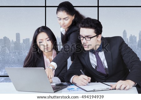 Image of woman leader team showing presentation on the laptop and her employees focus on the laptop with winter background on the window