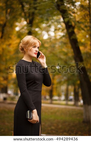 beautiful girl in a black dress talking on the phone at the park at autumn