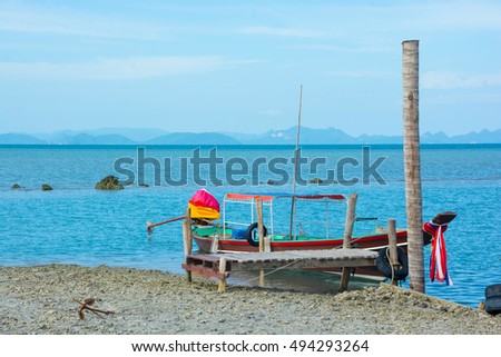 LONG TAIL BOAT DROPPED ANCHOR AT ROCKY BEACH NEARBY WOODEN BRIDGE PIER , ISLAND AND BLUE SKY BACKGROUND