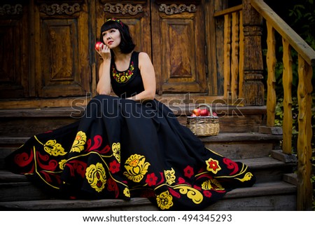 Portrait of beautiful girl sitting on the porch of an old house in national dress in the fall