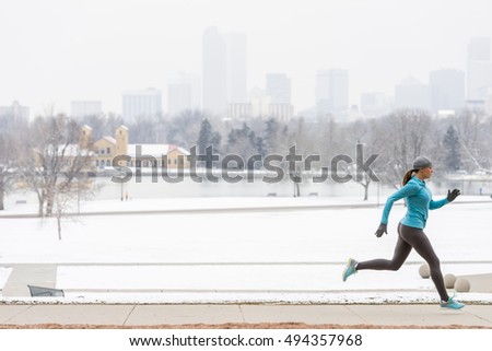 Young woman running jogging in snow blanketed City Park with Denver Colorado skyline in background