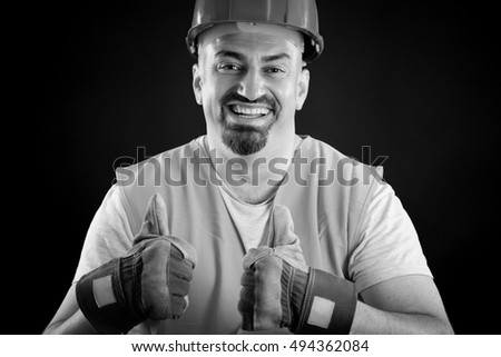 Portrait of a construction worker with hardhat and orange reflective vest making thumbs up sign. Black & white picture.