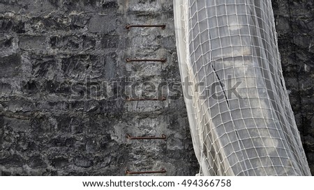 fire ladder on a wall built of black bricks and a pipe covered by white net
