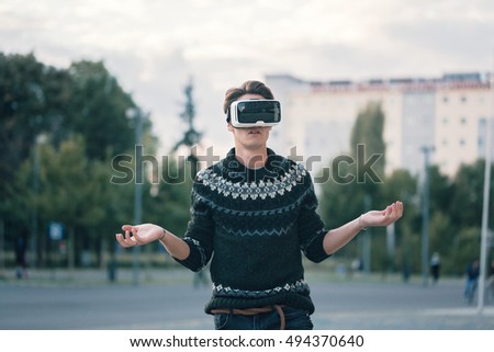 Curious young man with one pair of virtual reality glasses in a cool sweater and trendy outfit disappointed by augmented reality sunlit by sunset wondering about virtual app