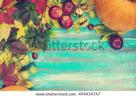 Frame made of autumn leaves, pumpkins, apples, chestnuts and wild grapes on old wooden background. Copy space. Toned image.