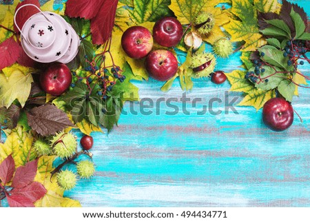 Frame made of autumn leaves, lamp, apples, chestnuts and wild grapes on old wooden background. Copy space. Top view.