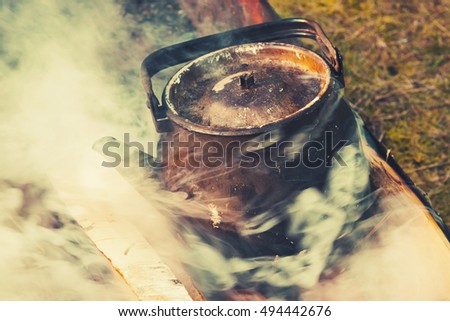 Old used teapot with boiling water stands on a bonfire, retro stylized photo with tonal correction filter effect, old instagram style