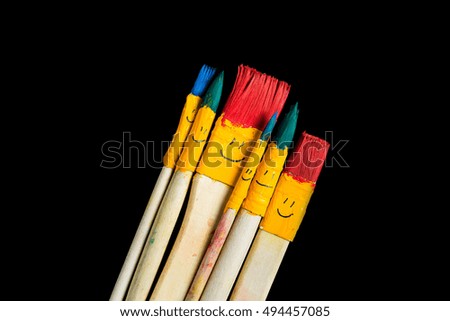 Colored brushes smile fun and happy. Brushes round and his hair colored in red, blue and emerald. Brushes like a toy family on a wood table. Isolated over black.
