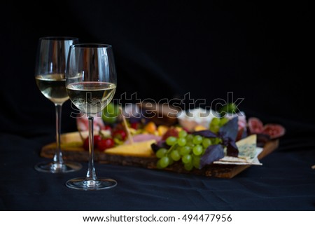 Two white wine glasses and cheese platter with fruits and meat