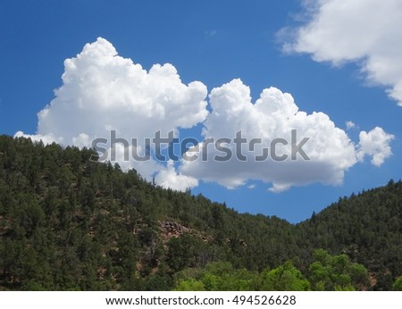 Picture clouds in a blue sky over a forested saddle; Tonto Natural Bridge State Park in Arizona
