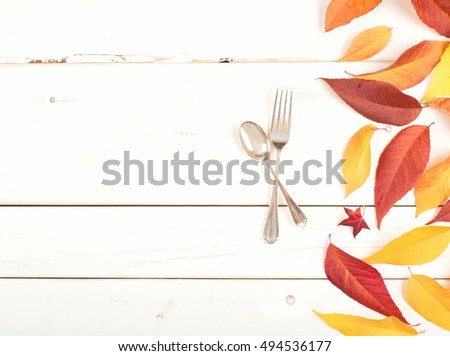 Pretty Fall Table Setting with Colorful Leaves and a fork and spoon from above on Rustic Painted White Board Background.  It's Simple and Casual with blank room or space for copy, text, your words.
