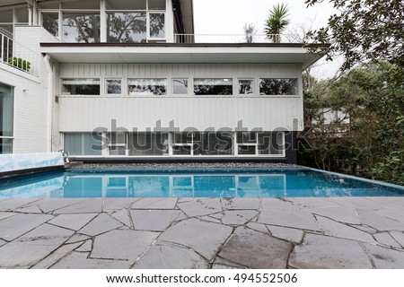 White weatherboard mid century home with in ground swimming pool and crazy paving