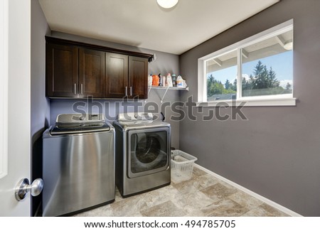 Grey laundry room with modern stainless steel washing machine and dryer, brown cabinets and  tile floor. Northwest, USA