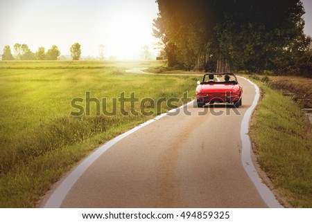Classic red convertible car traveling in the countryside at sunset Royalty-Free Stock Photo #494859325