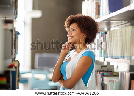 education, high school, university, learning and people concept - happy smiling african american student girl looking for or choosing book at library