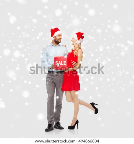 people, shopping, christmas, winter and holidays concept - happy couple in santa hats with red sale sign hugging over snow background